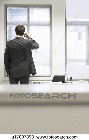 Businessman standing by desk in office Talking on Cell Phone View Large Photo Image Stock Image - Businessman standing by desk in office Talking on Cell Phone. Fotosearch