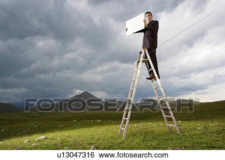 Businessman Standing on a Ladder in mountain field holding sign View Large Photo Image Stock Photograph - Businessman Standing on a Ladder in mountain field holding sign. Fotosearch