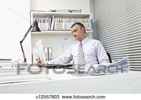 Stock Image - Businessman using laptop at office desk. Fotosearch