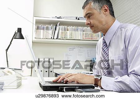 Businessman using laptop at office desk View Large Photo Image Stock Image - Businessman using laptop at office desk. Fotosearch