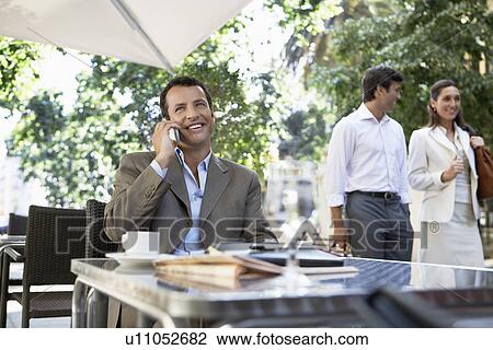 Stock Image - Businessman using mobile phone at outdoor cafe. Fotosearch