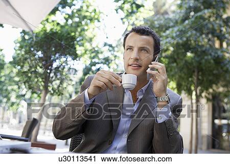 Stock Image - Businessman using mobile phone at outdoor cafe. Fotosearch