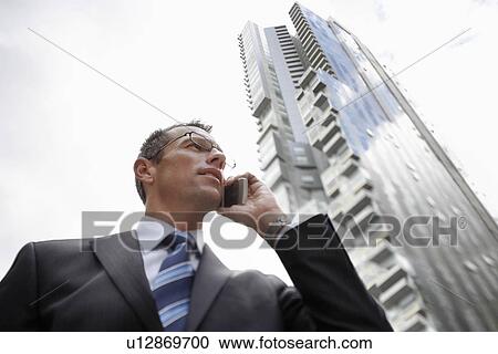 Businessman using mobile phone in front of tall building low angle view View Large Photo Image Stock Image - Businessman using mobile phone in front of tall building low angle view. Fotosearch
