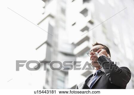 Businessman using mobile phone in front of tall building low angle view View Large Photo Image Stock Image - Businessman using mobile phone in front of tall building low angle view. Fotosearch