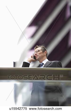 Businessman using mobile phone in front of building low angle view View Large Photo Image Stock Photography - Businessman using mobile phone in front of building low angle view. Fotosearch