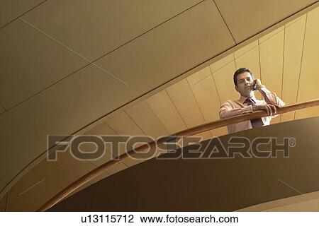 Businessman using mobile phone leaning on railing low angle view. View Large Photo Image Stock Image - Businessman using mobile phone leaning on railing low angle view.. Fotosearch