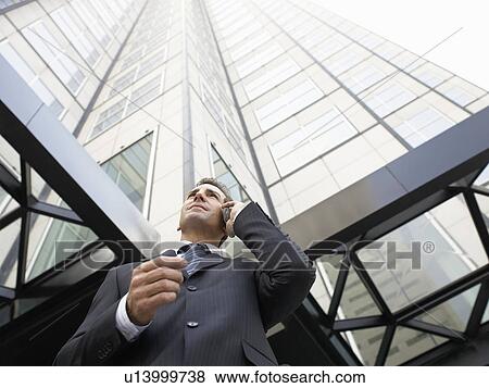 Businessman using mobile phone outside office (low angle view) View Large Photo Image Stock Photo - Businessman using mobile phone outside office (low angle view). Fotosearch