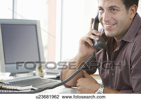 Businessman using telephone at desk in office View Large Photo Image Stock Image - Businessman using telephone at desk in office. Fotosearch
