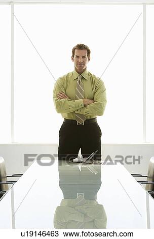Stock Image - Businessman with arms crossed at conference table portrait. Fotosearch
