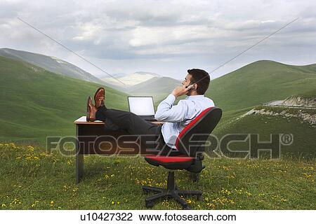 Businessman with feet on desk in mountain field talking on phone side view View Large Photo Image Stock Image - Businessman with feet on desk in mountain field talking on phone side view. Fotosearch
