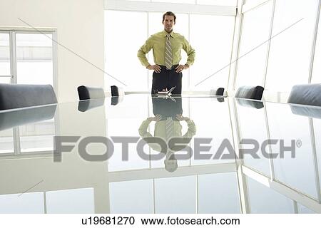 Stock Image - Businessman with hands on hips at conference table portrait. Fotosearch