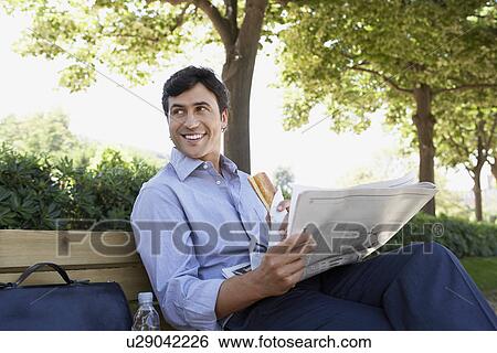 Businessman with sandwich and newspaper sitting on park bench View Large Photo Image Stock Photograph - Businessman with sandwich and newspaper sitting on park bench. Fotosearch