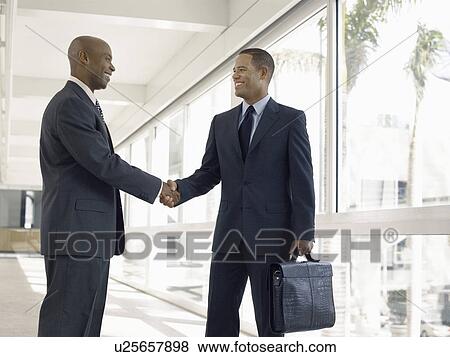 Stock Photo - Businessmen shaking hands in hallway. Fotosearch