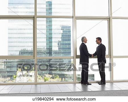 Picture - Businessmen shaking hands in office building. Fotosearch