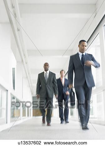 Stock Image - Businessmen walking down corridor (low angle view). Fotosearch