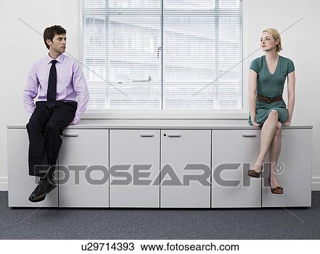 Stock Image - Businesspeople sitting on office cabinets. Fotosearch