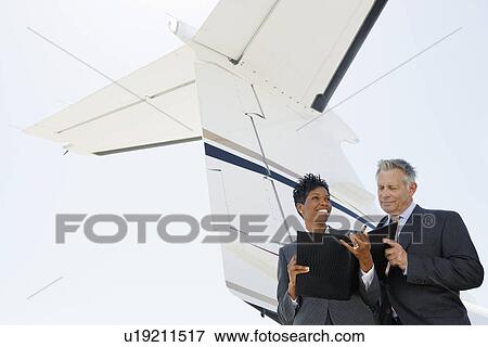Stock Photo - Businesspeople standing below wing of private jet low angle view. Fotosearch