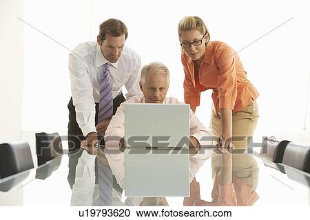 Stock Image - Businesspeople using laptop in conference room. Fotosearch