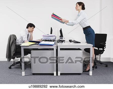 Stock Image - Businesswoman passing off work to male colleague in office. Fotosearch