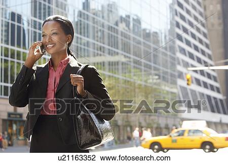 Stock Image - Businesswoman using mobile phone in street. Fotosearch