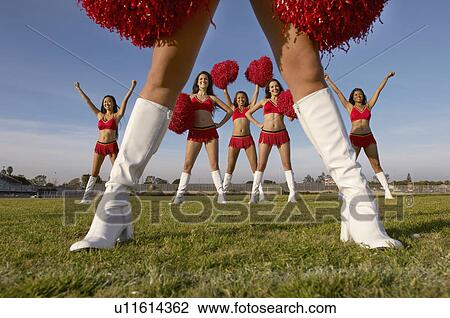 Stock Image - Cheerleader in white knee high boots low section with cheerleaders behind. Fotosearch