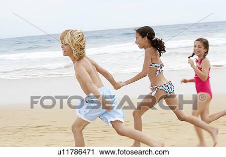 Children holding hands running along sandy beach side view View Large Photo Image Stock Image - Children holding hands running along sandy beach side view. Fotosearch