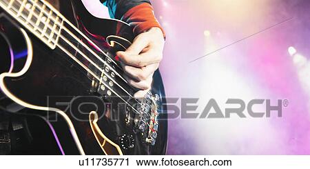 Stock Image - Close-up of man playing bass guitar at concert mid section. Fotosearch