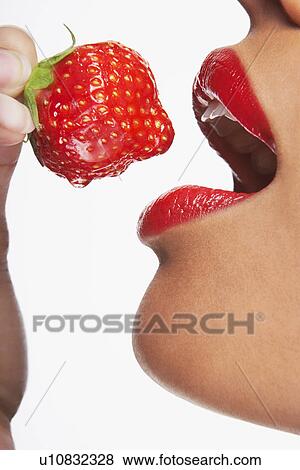 Stock Photo - Close up of woman with shiny red lips about to bite into a juicy strawberry. Fotosearch