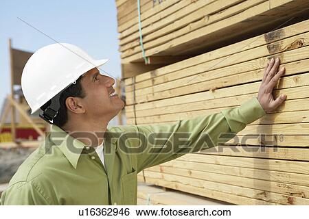 Construction Worker in hard hat inspecting Lumber on job site side view View Large Photo Image Stock Photograph - Construction Worker in hard hat inspecting Lumber on job site side view. Fotosearch