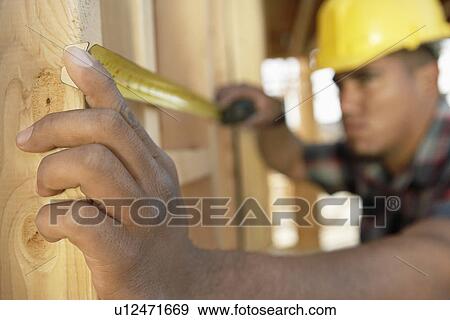 Stock Photo - Construction Worker measuring between boards with tape measure on construction Site. Fotosearch