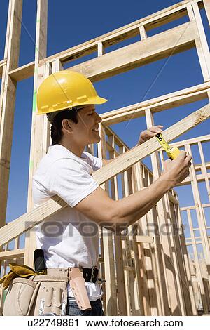 Construction worker measuring lumber at construction site View Large Photo Image Stock Image - Construction worker measuring lumber at construction site. Fotosearch