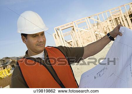 Construction worker standing on construction site and holding blueprints View Large Photo Image Stock Image - Construction worker standing on construction site and holding blueprints. Fotosearch