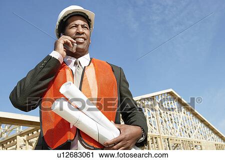 Stock Image - Construction Worker wearing hard hat Using Cell Phone on construction site. Fotosearch