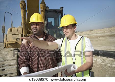 Construction Workers wearing hard hats standing in front of heavy equipment looking at plan View Large Photo Image Stock Image - Construction Workers wearing hard hats standing in front of heavy equipment looking at plan. Fotosearch
