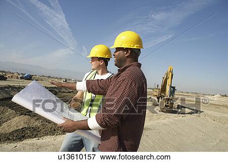 Stock Photo - Construction Workers wearing hard hats looking at plan on Site. Fotosearch