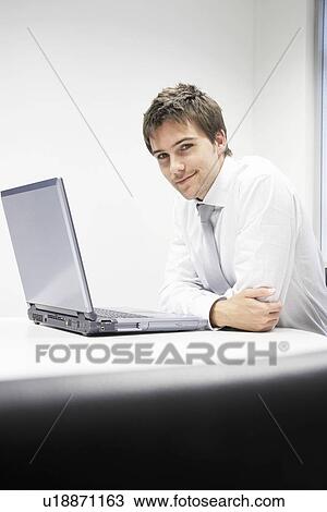 Contented Businessman sitting at desk with Laptop portrait View Large Photo Image Stock Image - Contented Businessman sitting at desk with Laptop portrait. Fotosearch