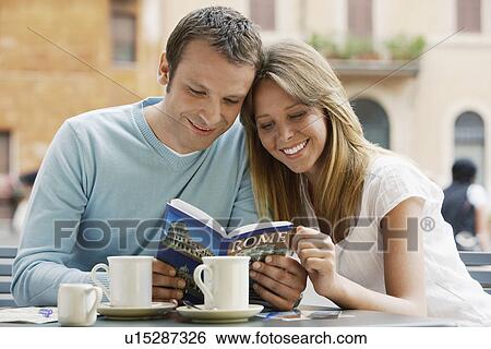 Stock Photograph - Couple at outdoor cafe looking at guidebook of Rome front view. Fotosearch