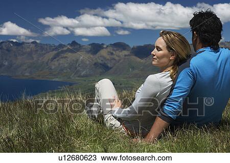 Stock Image - Couple cuddling looking over lake and hills. Fotosearch