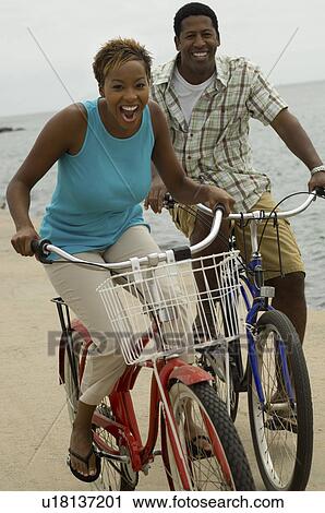 Stock Image - Couple cycling on beach smiling. Fotosearch