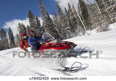 Stock Photo - Couple driving snowmobile through snow. Fotosearch