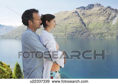 Couple embracing looking at mountain lake View Large Photo Image Stock Photo - Couple embracing looking at mountain lake. Fotosearch