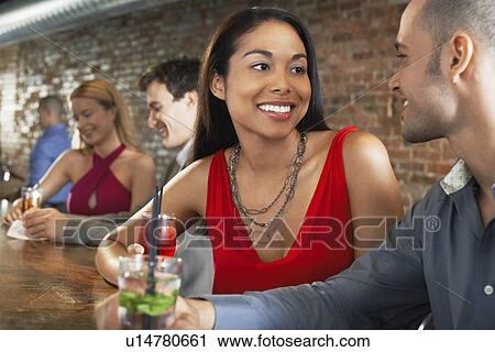 Couple holding cocktails sitting at bar View Large Photo Image Stock Image - Couple holding cocktails sitting at bar. Fotosearch