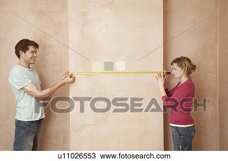 Stock Image - Couple holding measuring tape to wall in unrenovated room. Fotosearch