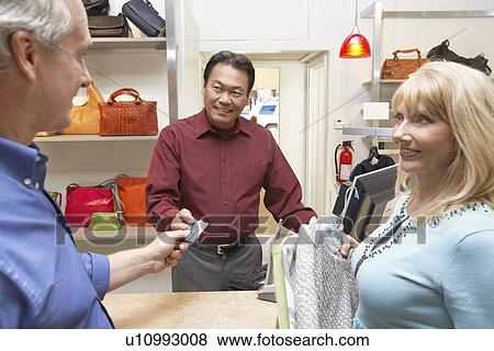 Couple in clothing store husband giving credit card to sales clerk View Large Photo Image Stock Photo - Couple in clothing store husband giving credit card to sales clerk. Fotosearch