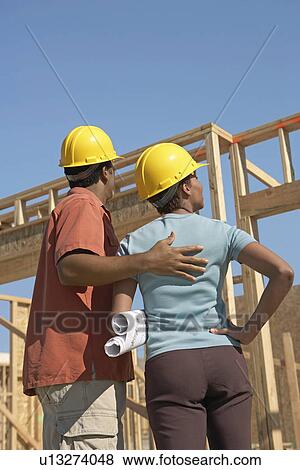 Couple in hard hats on building site back view View Large Photo Image Stock Photo - Couple in hard hats on building site back view. Fotosearch