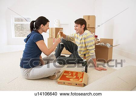 Stock Image - Couple in new home toasting with champagne and pizza. Fotosearch