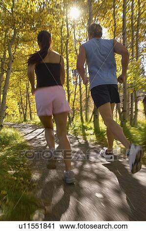 Stock Image - Couple jogging through woodland rear view. Fotosearch