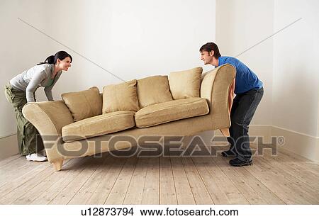 Picture - Couple lifting sofa in empty room. Fotosearch