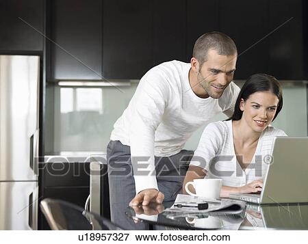 Couple looking at lap top in modern kitchen View Large Photo Image Stock Photo - Couple looking at lap top in modern kitchen. Fotosearch