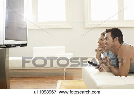 Couple lying on bed watching plasma TV together side view View Large Photo Image Stock Photo - Couple lying on bed watching plasma TV together side view. Fotosearch